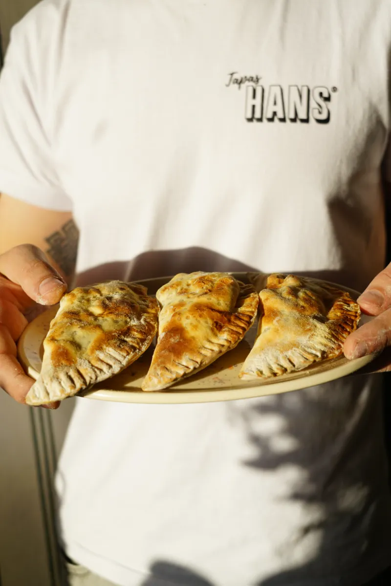 Persona con remera HANS sosteniendo un plato con tres empanadas doradas